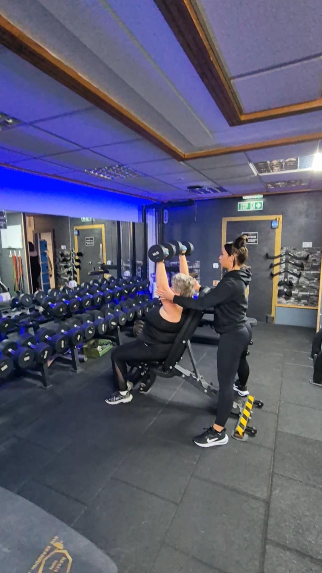 A coach supporting a member with a seated dumbbell press