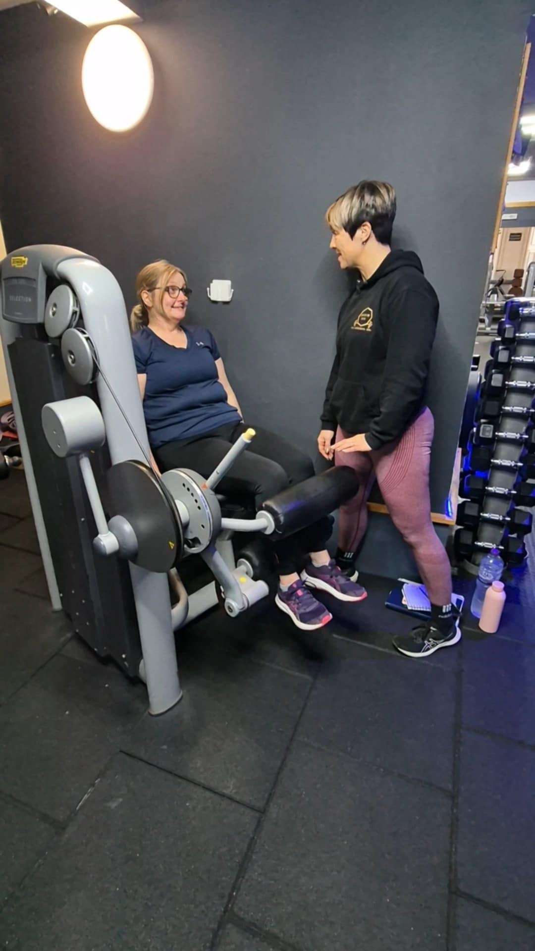 A coach and a seated member talking beside a gym strength machine